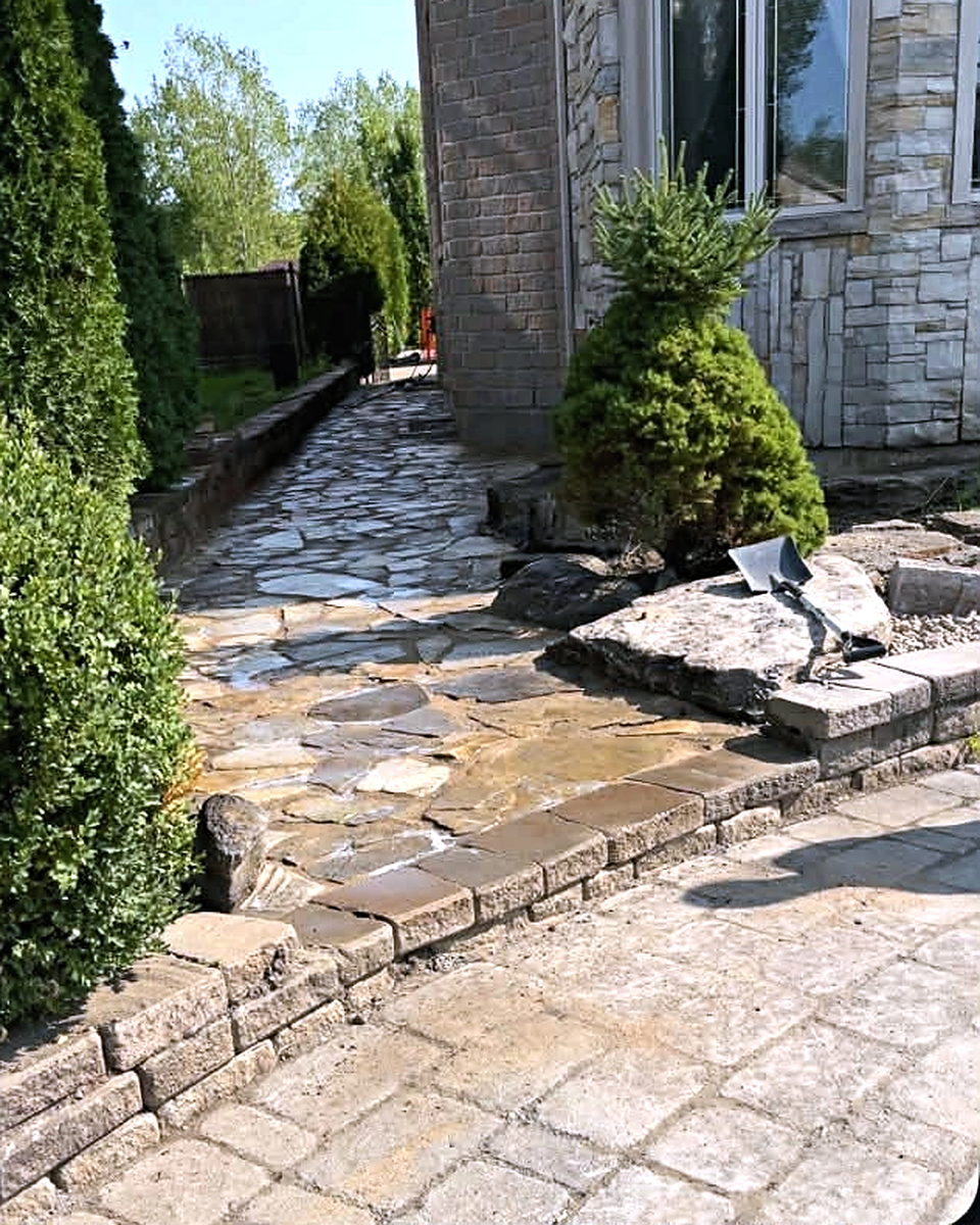 Après les travaux : allée en dalles de pierre naturelle posée entre la maison et la haie, raccordée à une terrasse en pavé.