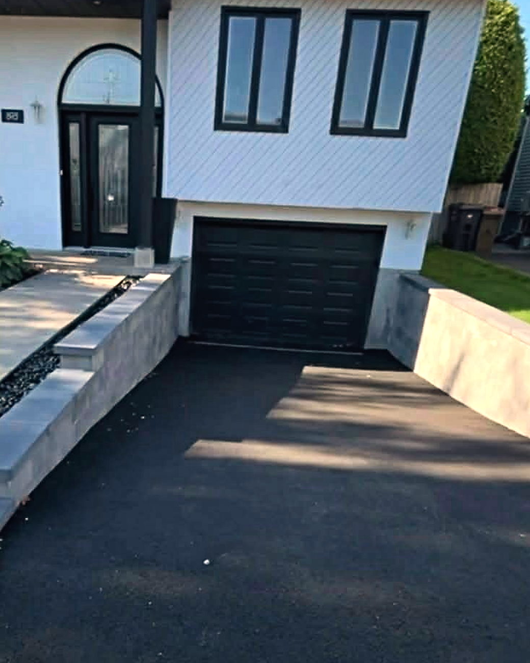 Après les travaux : murets de béton de chaque côté de l’entrée, escalier et allée en dalles vers la porte, et asphalte neuf.