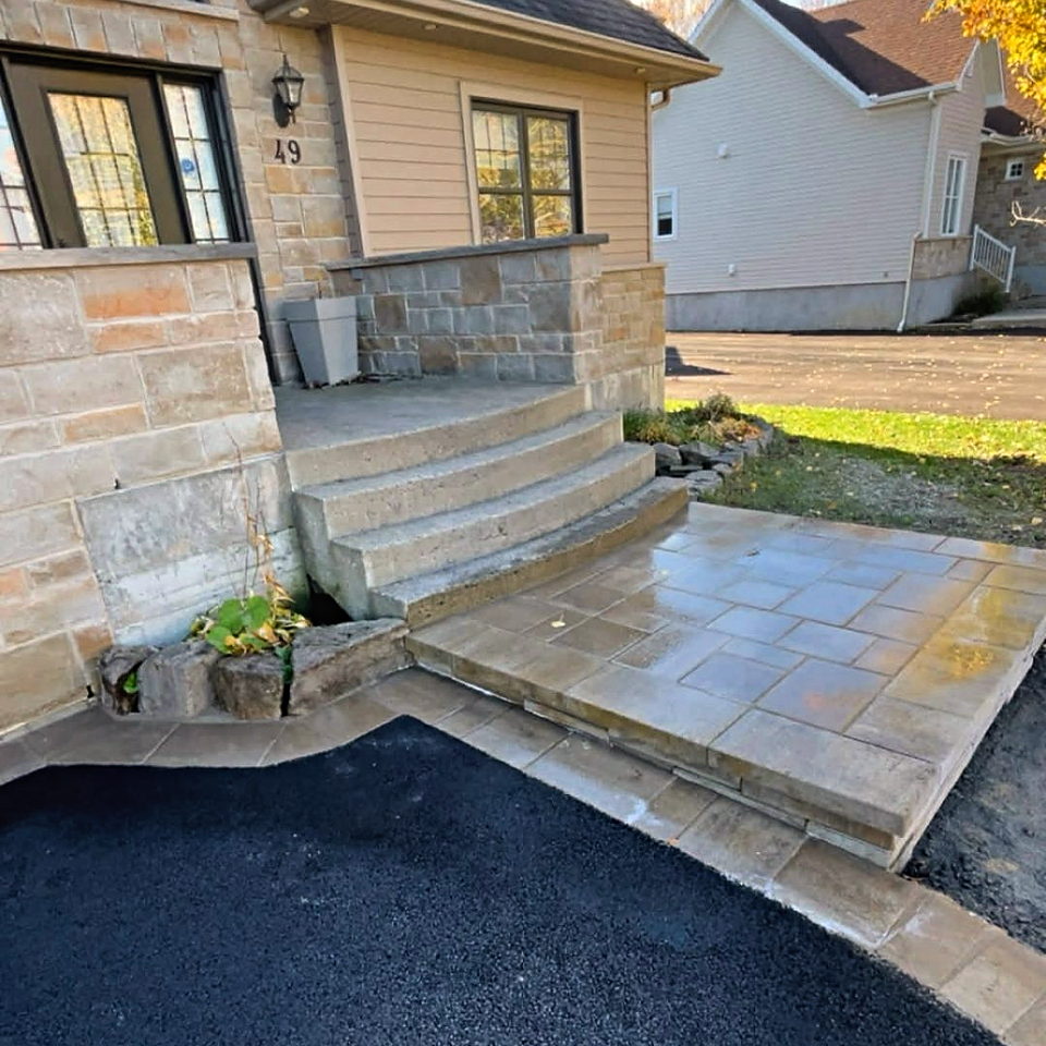 Palier en dalles de béton beige installé devant un escalier de béton arrondi, avec un stationnement en asphalte neuf à côté.